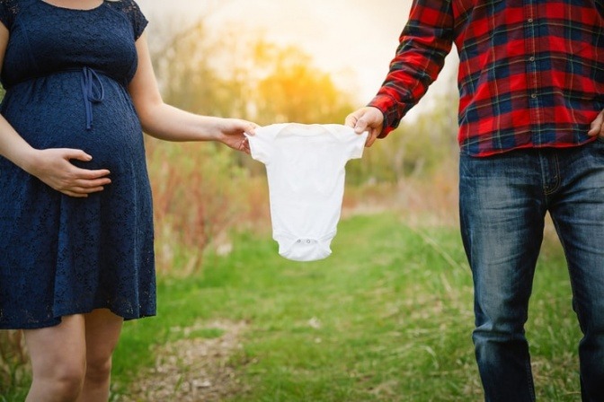 Zwei werdende Eltern halten einen weißen Babystrampler in ihrer Mitte