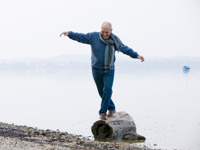 Ein älterer Mann balanciert auf einem Baumstamm