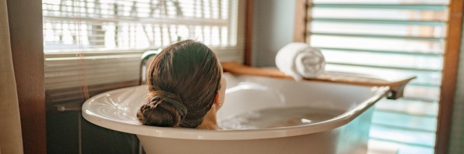 Eine Frau entspannt sich in der Badewanne, nachdem sie erfolgreich gelernt hat, wie man ein Basenbad selber machen kann.