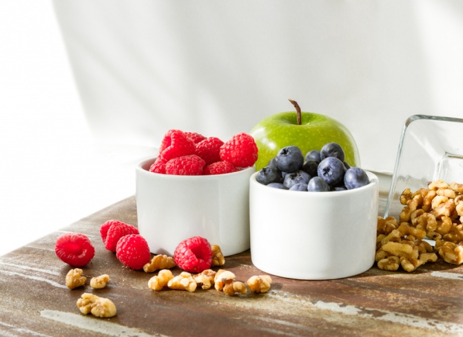 Beeren und Nüsse in einer Schüssel, daneben ein Apfel