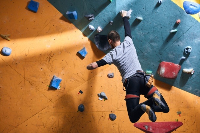 Mann mit einem Arm trainiert Klettern an einer Kletterwand.