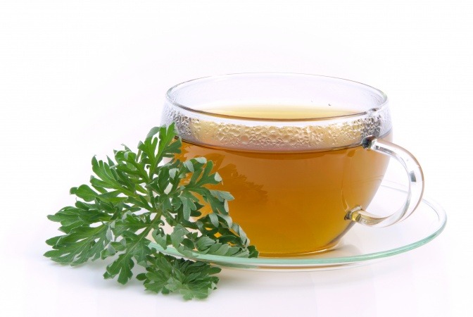 Eine Tasse mit Beifußtee, daneben Beifußblätter