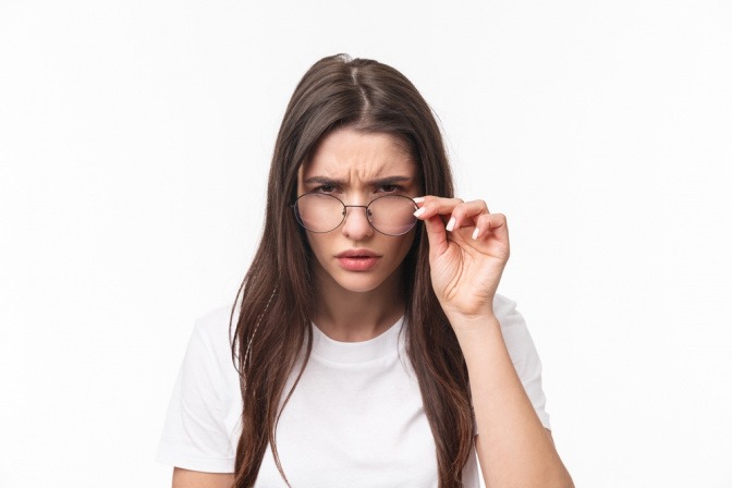 Junge Frau setzt Brille ab und hat kritischen, verurteilenden Blick.