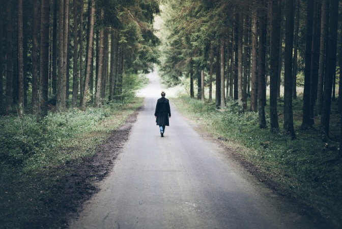 Frau läuft allein auf einer langen Straße durch einen Wald.