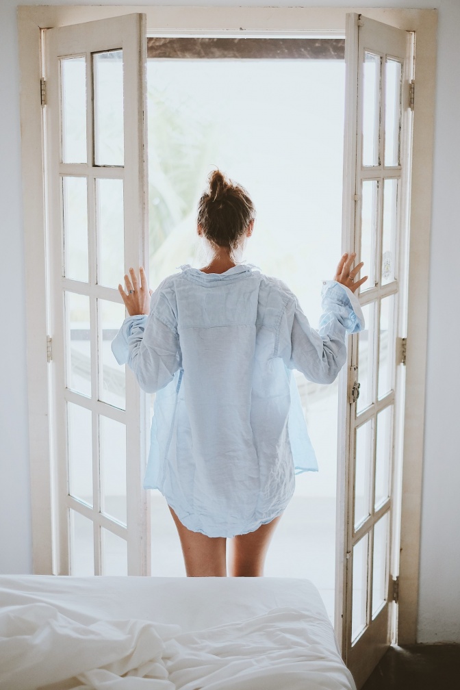 Eine Frau schaut vor dem Bett aus dem Fenster