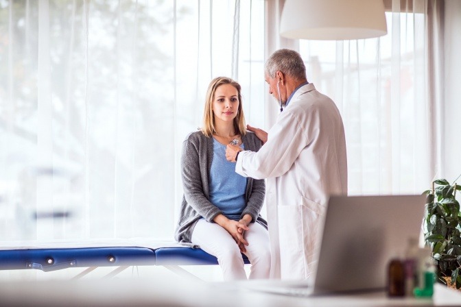 Eine Frau sitzt beim Arzt um eine Krankheit zu bewältigen