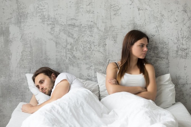 Ein Paar liegt im gemeinsamen Bett und wirkt distanziert; es hat Tipps zum Thema Beziehung beleben anscheinend dringend nötig.