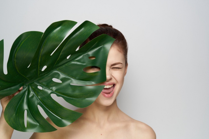 Eine Frau hält ein großes grünes Blatt vor ihr Gesicht