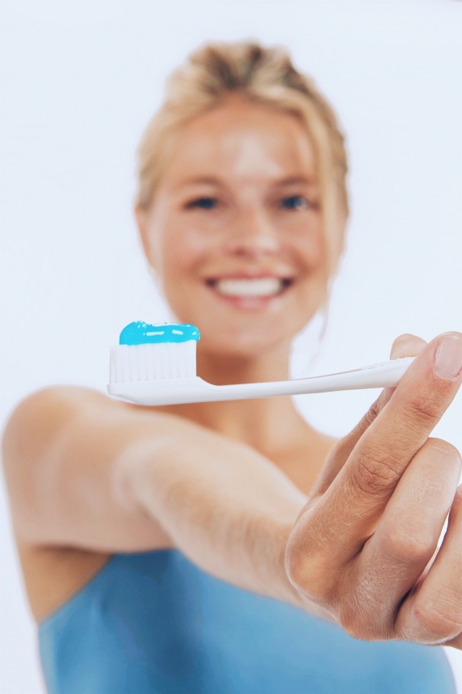 Eine blonde Frau hält eine Zahnbürste mit blauer Zahnpaste