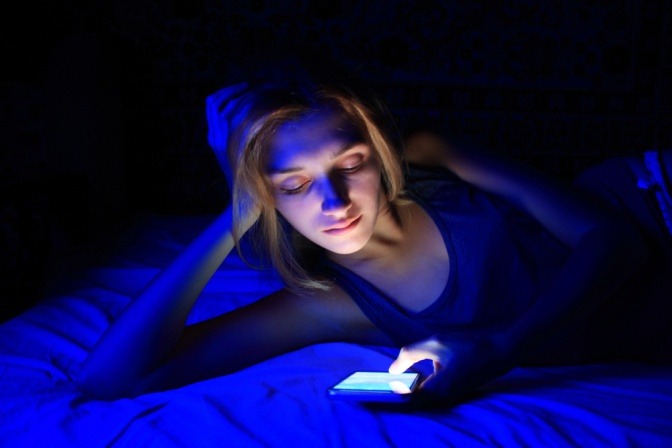 Frau liest nachts im Bett auf ihrem sehr hellen und blaulichtstarken Smartphone.