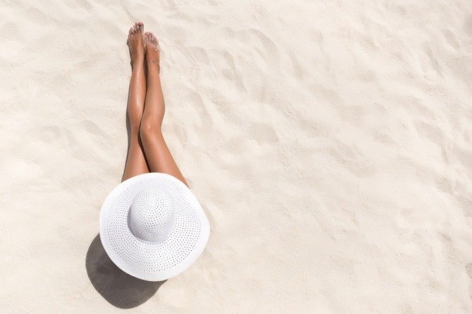 Frau mit Sonnenhut von oben am Strand. 
