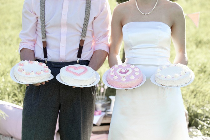 Braut und Bräutigam stehen nebeneinander, beide halten jeweils eine Torte in jeder Hand.