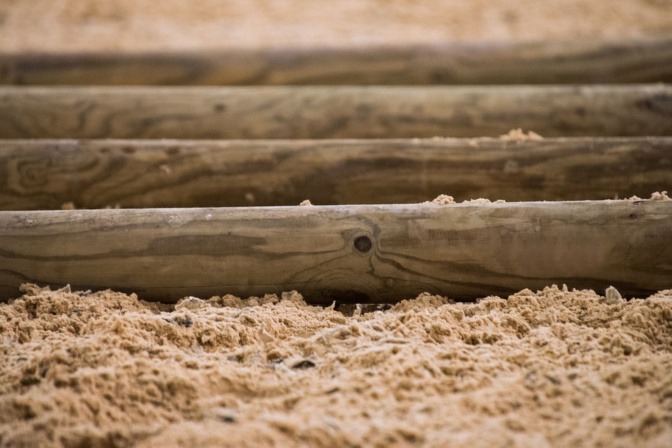 Auf einem sandigen Boden liegen mehrere Holzstangen hintereinander