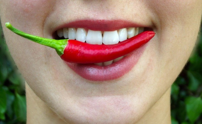 Lächelnder Frauenmund mit Chili zwischen den Zähnen.