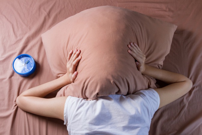 Frau liegt im Bett und hat das Kissen über den Kopf gezogen