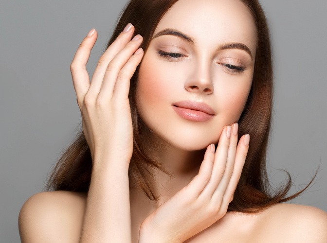 Frau hält ihre dezent mit dem Clean Nails Trend manikürten Nägel ins Gesicht. 