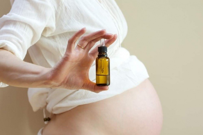 Eine schwangere Frau hält ein Fläschchen Dammöl in der Hand