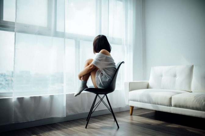 Eine Frau in depressiver Stimmung sitzt auf einem Stuhl beim Fenster