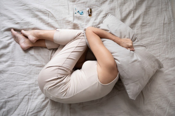 Eine Frau liegt im Bett und versteckt ihr Gesicht unter einem Kissen