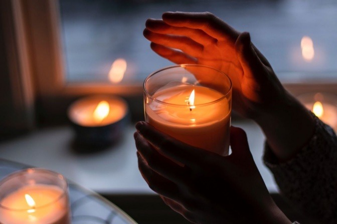 Eine Hand über einer Duftkerze, die warme Atmosphaere verbreitet