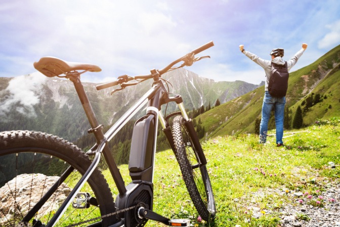 Ein Mann auf einem Berg steht triumphierend vor einem E-Bike