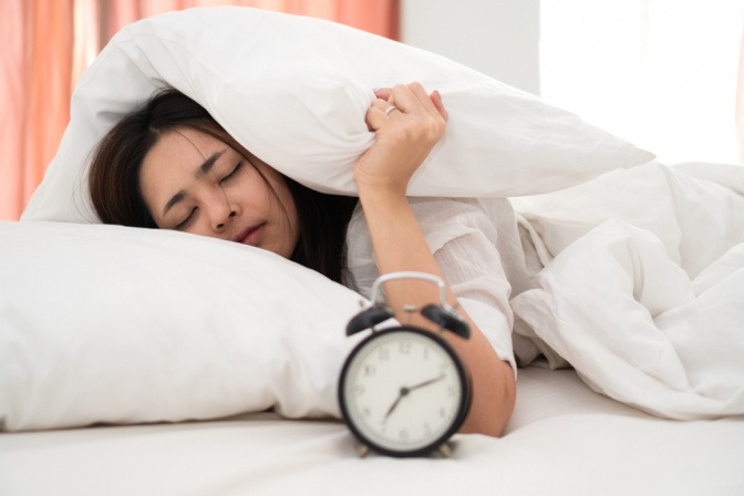 Verschlafene Frau will morgens nicht aus dem Bett aufstehen.