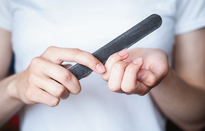 Eine Frau beugt eingerissenen Fingernägeln mit Nagelfeile vor