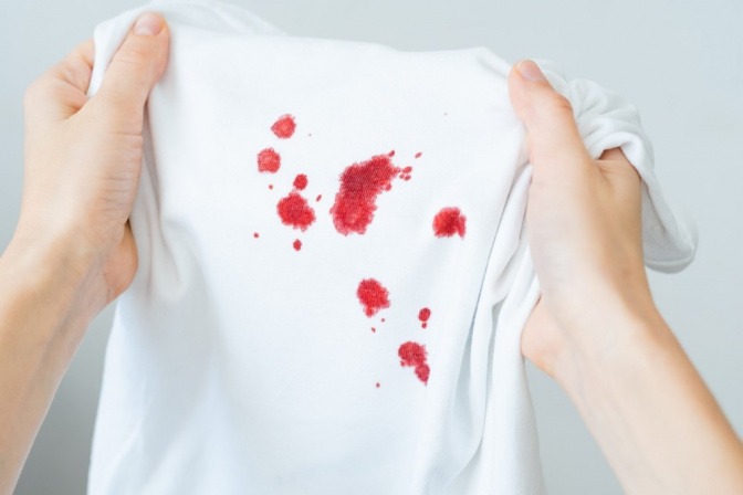 Frau hält Wäschestück mit frischen Blutflecken in den Händen.