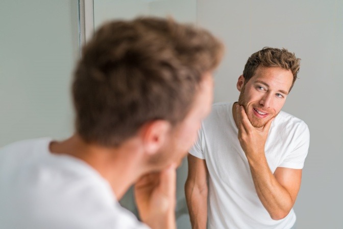 Mann prüft die Rasur vor dem Spiegel