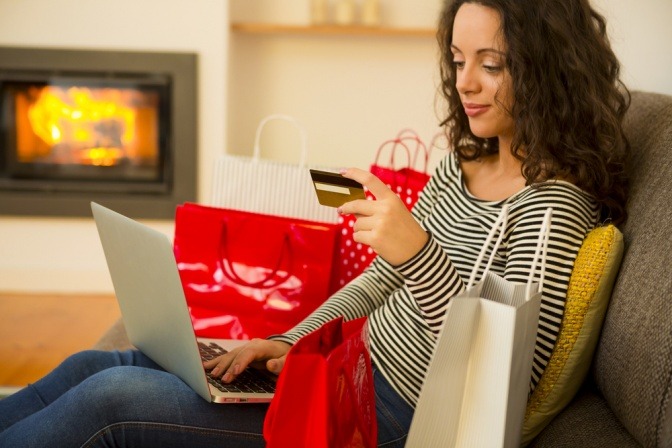 Eine Frau mit Kaufsucht sitzt am Sofa mit vielen Einkaufstaschen und bestellt mit Kreditkarte