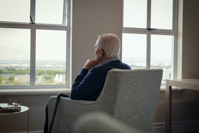 Eine älterer Mann sitzt auf einem Sessel und blickt aus dem Fenster