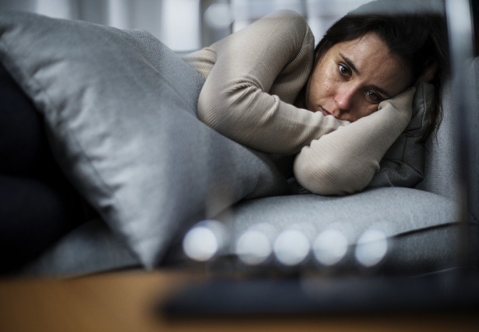 Eine Frau liegt niedergeschlagen auf der Couch