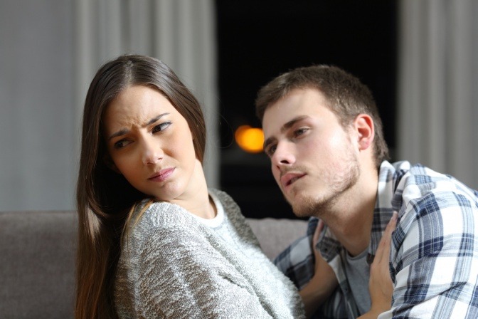 Eine Frau wendet sich angewindert von einem Mann ab, der versucht ihr auf der Couch näherzukommen 