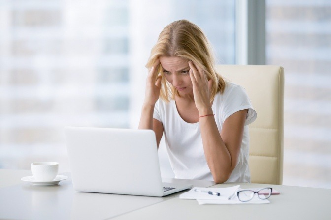 Frau vor Notebook wird durch Elektrosmog belastet und leidet unter Kopfschmerzen