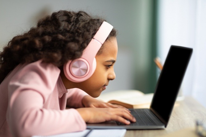 Junges Mädchen hat Kopfhörer auf und sitzt mit dem Gesicht ganz nah vor einem Laptop.