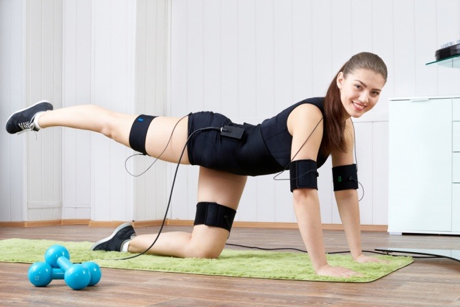 Eine Frau macht Übungen am Boden mit einem EMS-Gerät