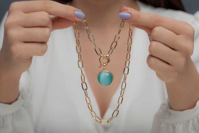 Frau hält goldene Energieschmuck-Kette mit Edelstein