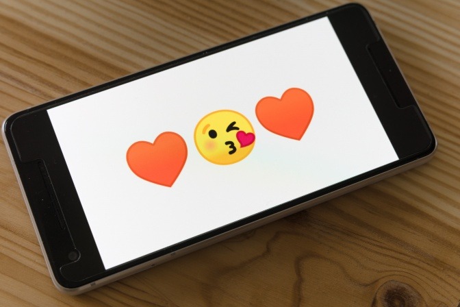 Ein Smartphone, auf dessen Bildschirm Smileys und ein Herzchen-Icon zu sehen sind.