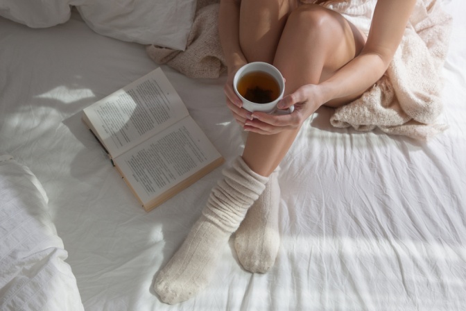 Frau mit einer Tasse Tee und einem Buch im Bett