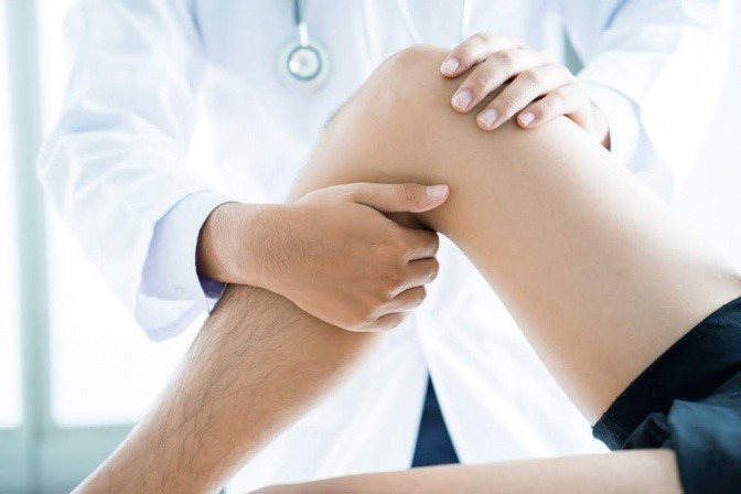 Ein gebeugtes Bein auf einer Arztliege, während ein Arzt es untersucht.