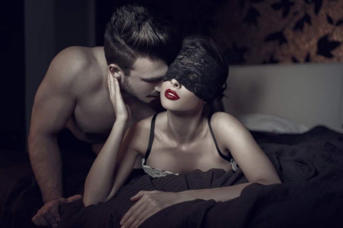 Eine Frau hat eine Augenmaske im Bett auf, der Mann verführt sie