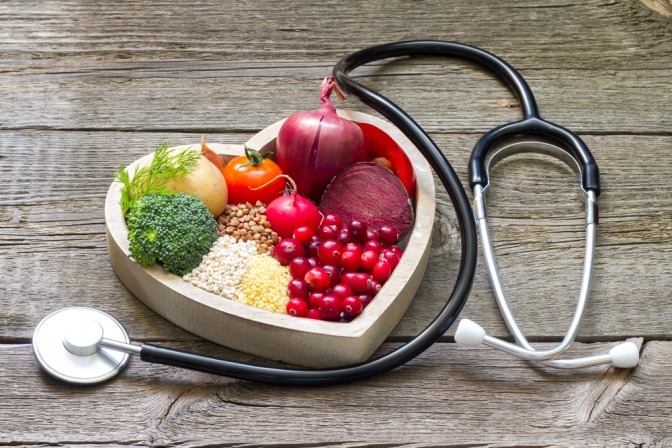 Essen zum Cholesterin senken liegt in einer Herzform, daneben ein Stetoskop