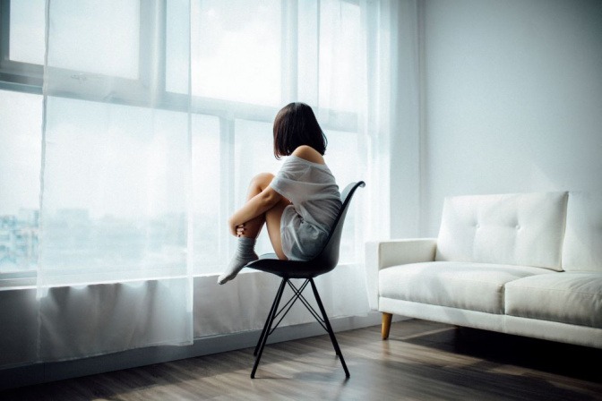 Eine Frau sitzt mit angezogenen Beinen in einem leeren Raum
