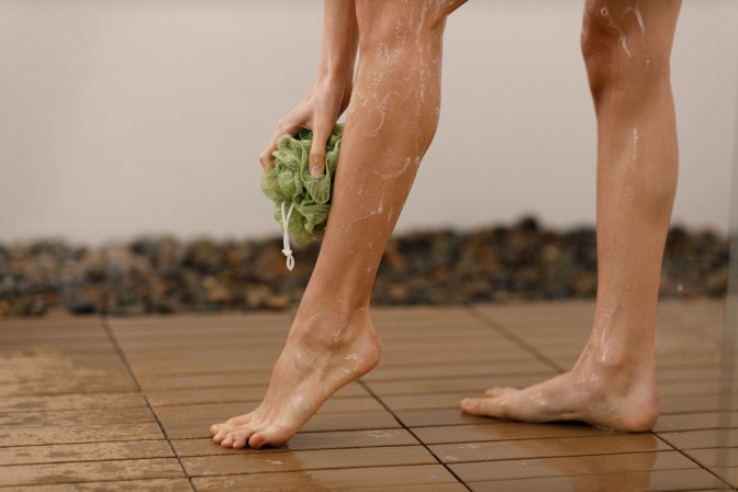 Eine Frau wäscht ihre Beine unter der Dusche mit einem Schwamm.