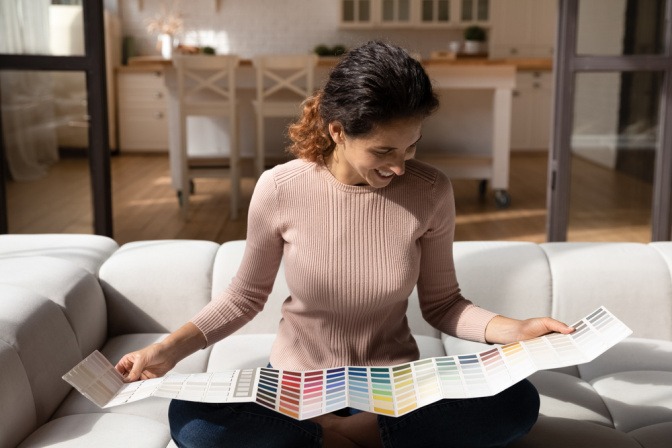 Eine lachende Frau sitzt auf der Couch und schaut sich verschiedene Farben an