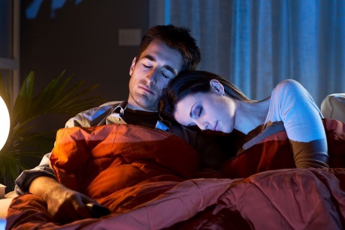 Ein Paar liegt im Bett, die Frau ist an den Arm ihres Partners gelehnt und schläft.