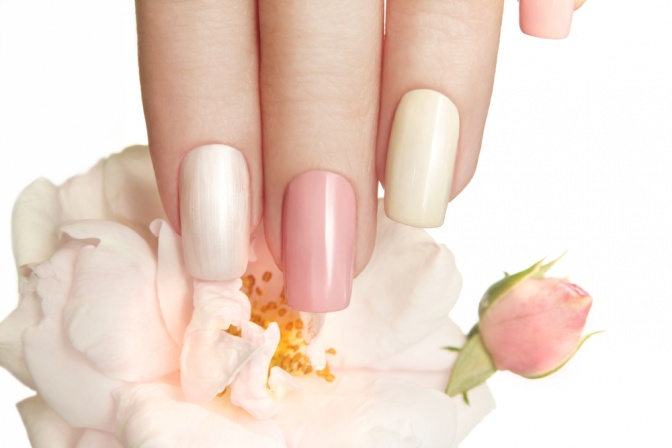 Eine Hand mit weiß und rosa lackierten Nägeln hält eine rosa Blume