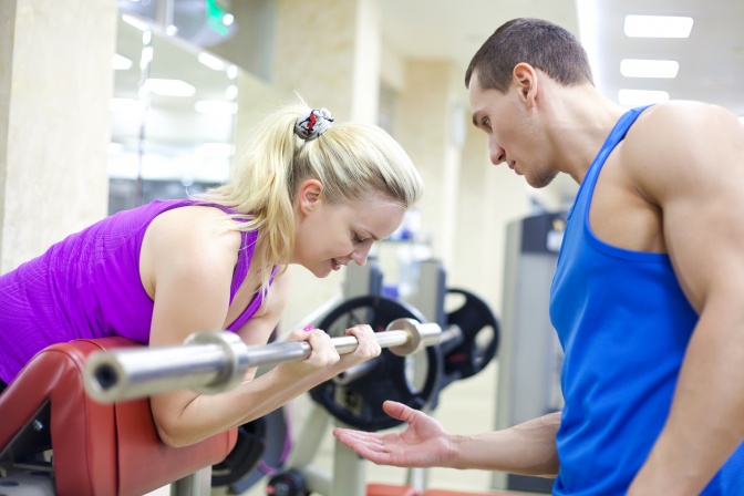 Ein Fitnesstrainer hilft einer Frau bei einer Hantel