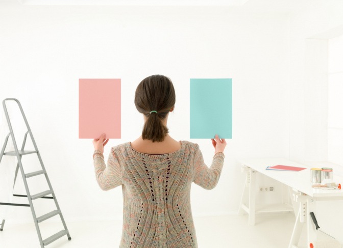 Eine Frau in einem weißen Raum hält zwei Farbtafeln in der Hand