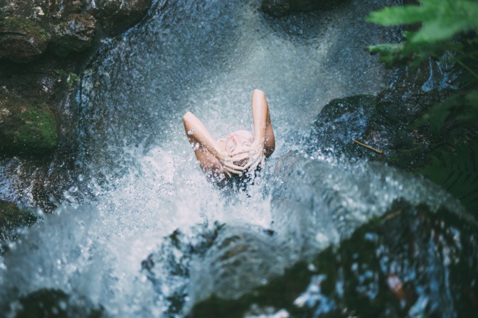 Frau duscht kalt unter einem Wasserfall